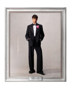 Young man in a black tuxedo with bow tie and pink boutonniere stands with hands in pockets, framed as a formal portrait labeled Rubacuori.