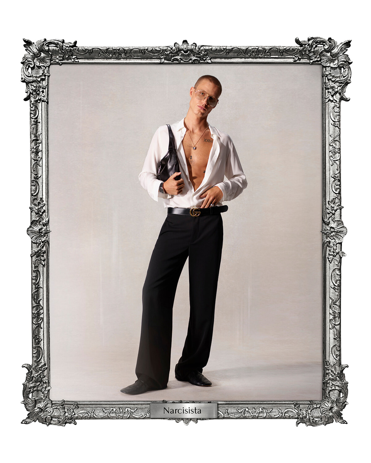 Male model in an open white shirt, black wide-leg pants, sunglasses, and a shoulder bag, posed in a decorative frame labeled Narcisista.