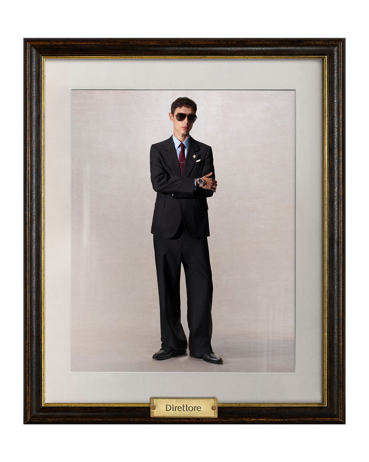 Portrait of a man in a black suit and sunglasses, arms crossed, framed with a bottom plaque reading Direttore.