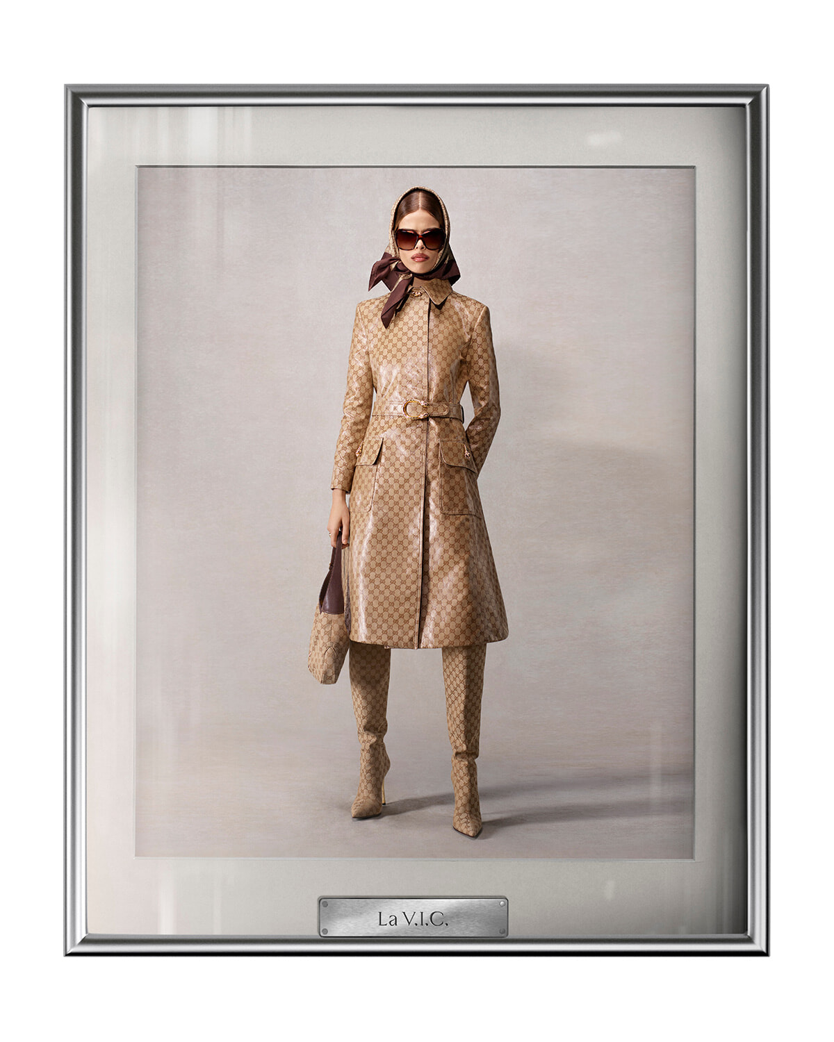 Model wearing a beige patterned belted trench coat with matching boots, scarf, sunglasses, and handbag in a framed studio portrait labeled La V.I.C.