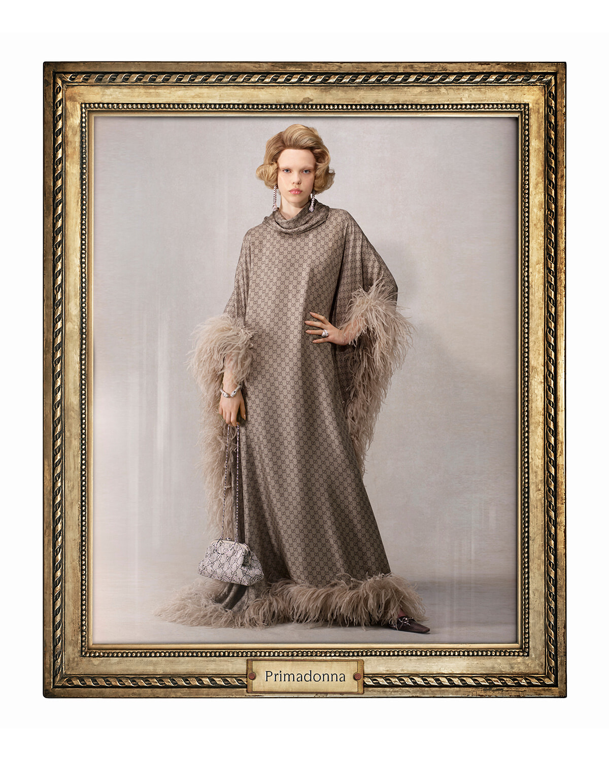 Framed studio portrait of a woman in a grey patterned gown with feathered cuffs and hem, holding a small purse; Primadonna label at bottom frame.
