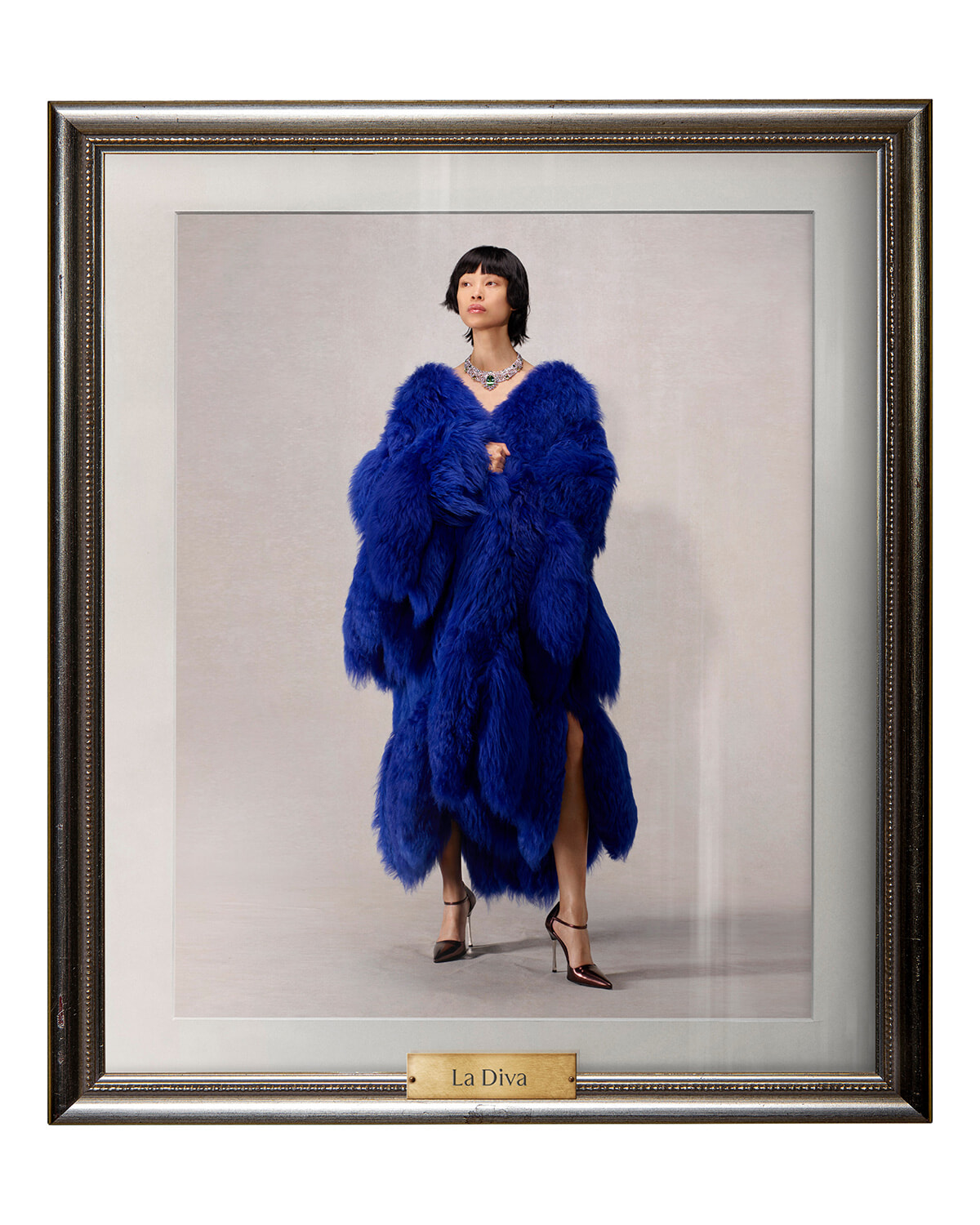 Portrait of a woman in a vivid blue fur coat, standing in a decorative frame with a 'La Diva' plaque beneath the image.