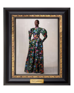 Portrait of a woman in a long, vibrant floral gown, standing with hands on hips inside a black and gold ornate frame, titled 'La Contessa'