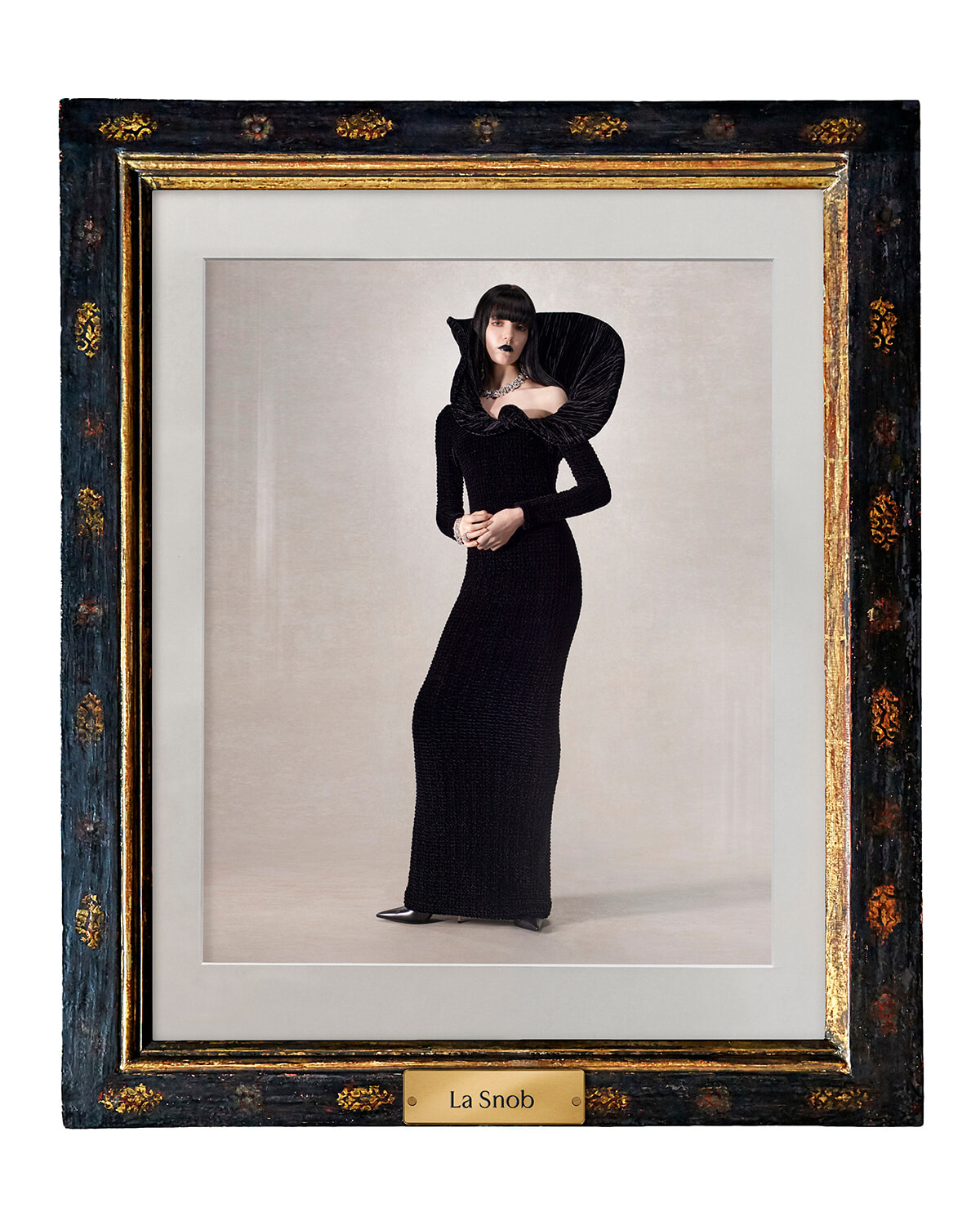 Portrait of a woman in a floor-length black textured gown with a dramatic oversized collar, posed inside a dark ornate frame labeled La Snob.