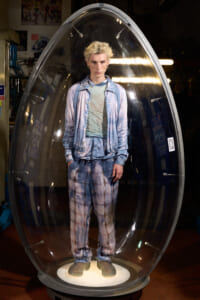 Mannequin wearing a light blue denim-inspired outfit inside a clear egg-shaped display pod, standing on a lit pedestal in a store.