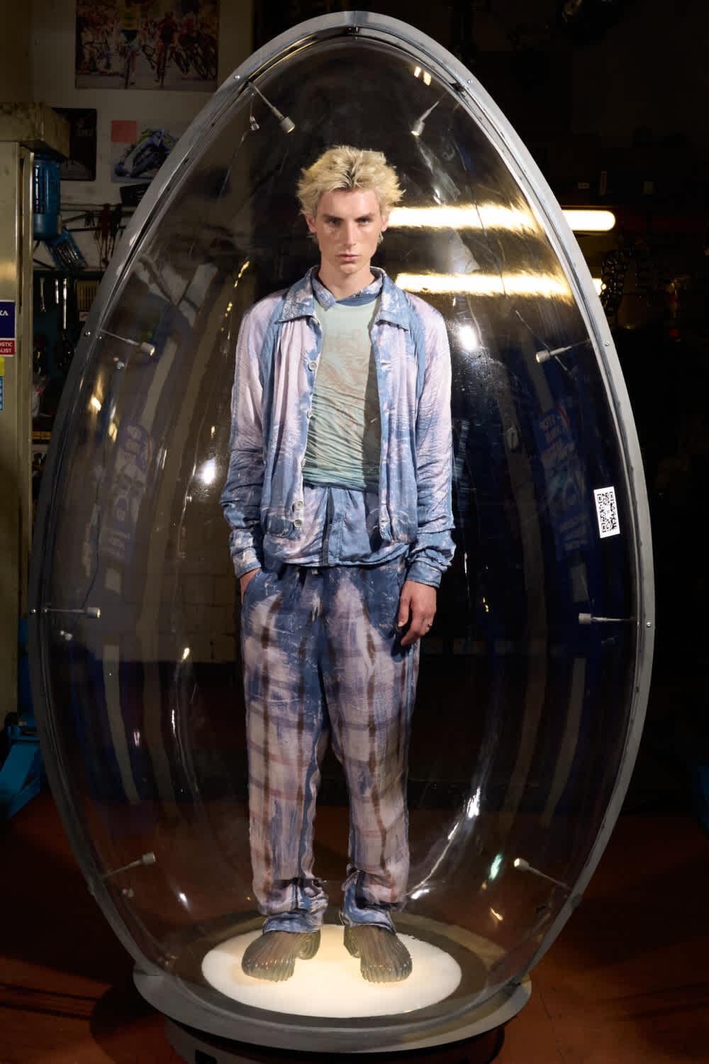 Mannequin wearing a light blue denim-inspired outfit inside a clear egg-shaped display pod, standing on a lit pedestal in a store.