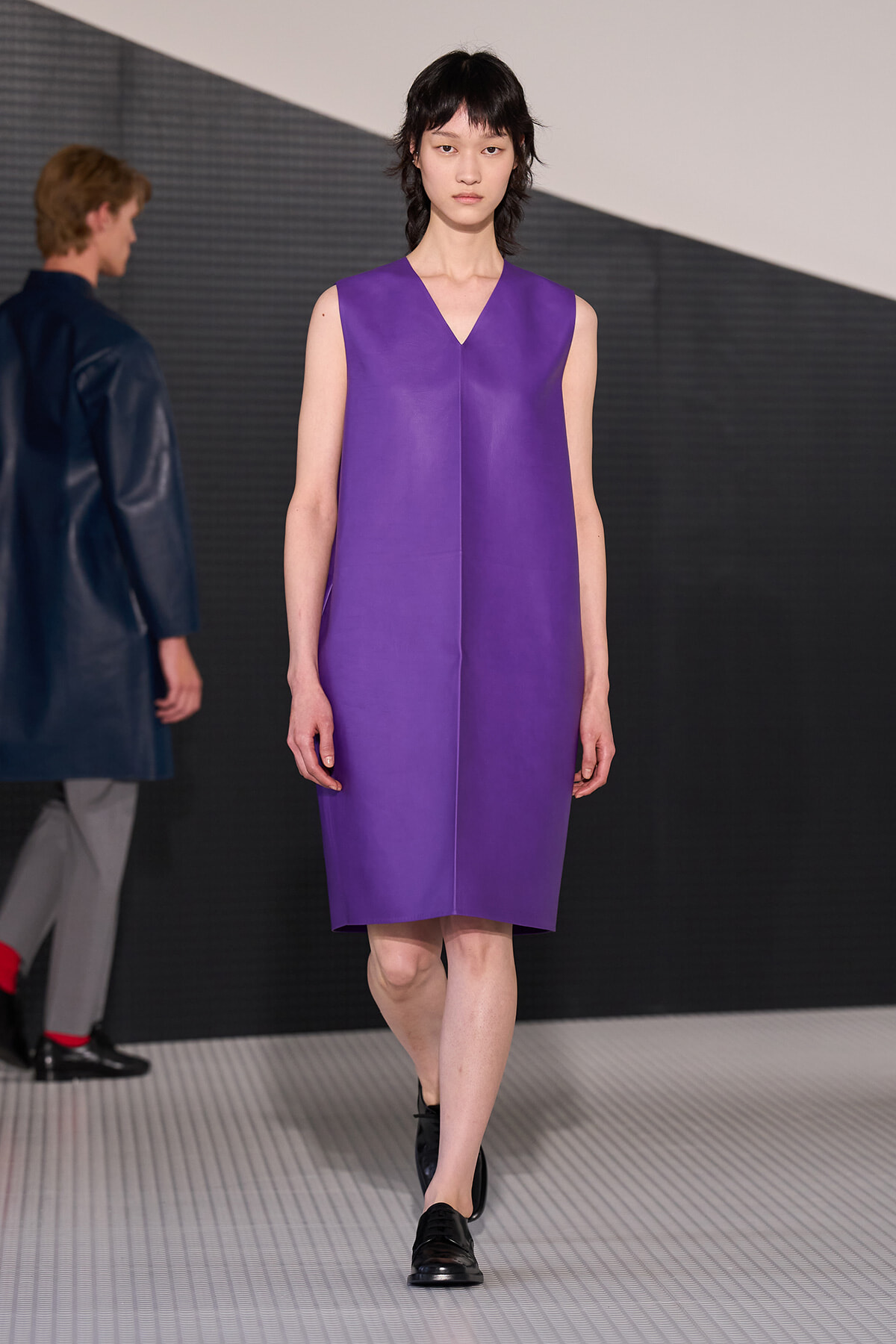 Model walking the runway in a sleeveless, violet V-neck shift dress with black loafers.