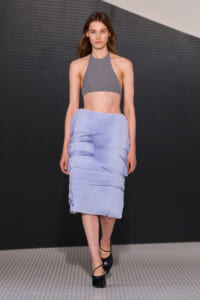 Female model walking a runway in a gray halter crop top and a light blue tiered ruched midi skirt.