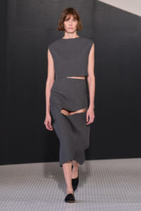 Model walks the runway in a gray cropped sleeveless top with a matching high-waisted skirt featuring cut-out sections and black flats.