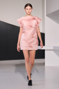 Female model wearing a soft pink, textured mini dress walking down a fashion runway.