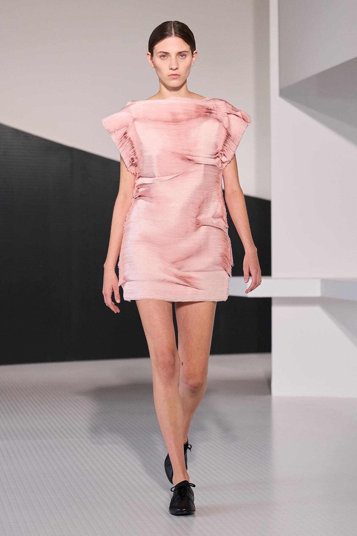 Female model wearing a soft pink, textured mini dress walking down a fashion runway.