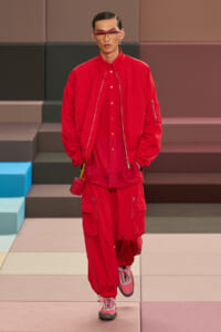 Model wearing an all-red streetwear outfit: oversized bomber jacket, red shirt and cargo pants, pink sneakers, and a small red bag.