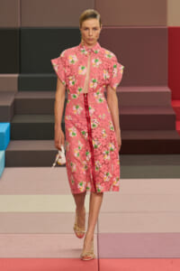 Runway model in a pink floral lace midi dress with a red center zipper, walking on a multicolor stepped runway.
