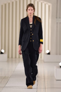 Female model walking a runway in a navy suit with gold buttons and tan shoes