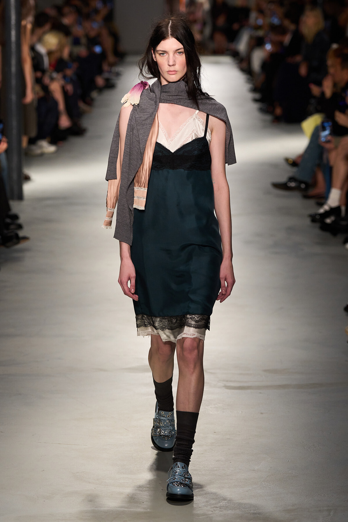 Model walks the runway in a teal satin slip dress with cream lace trim, layered under a pinkish slip, and a gray scarf draped over one shoulder.