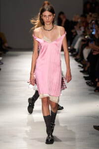 Models walks a pink satin slip dress with cream lace underlayer down a runway, pairing with dark socks and patent shoes.