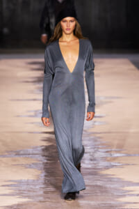 Model walks the runway in a metallic blue-grey deep-V gown with long sleeves and a black headscarf.