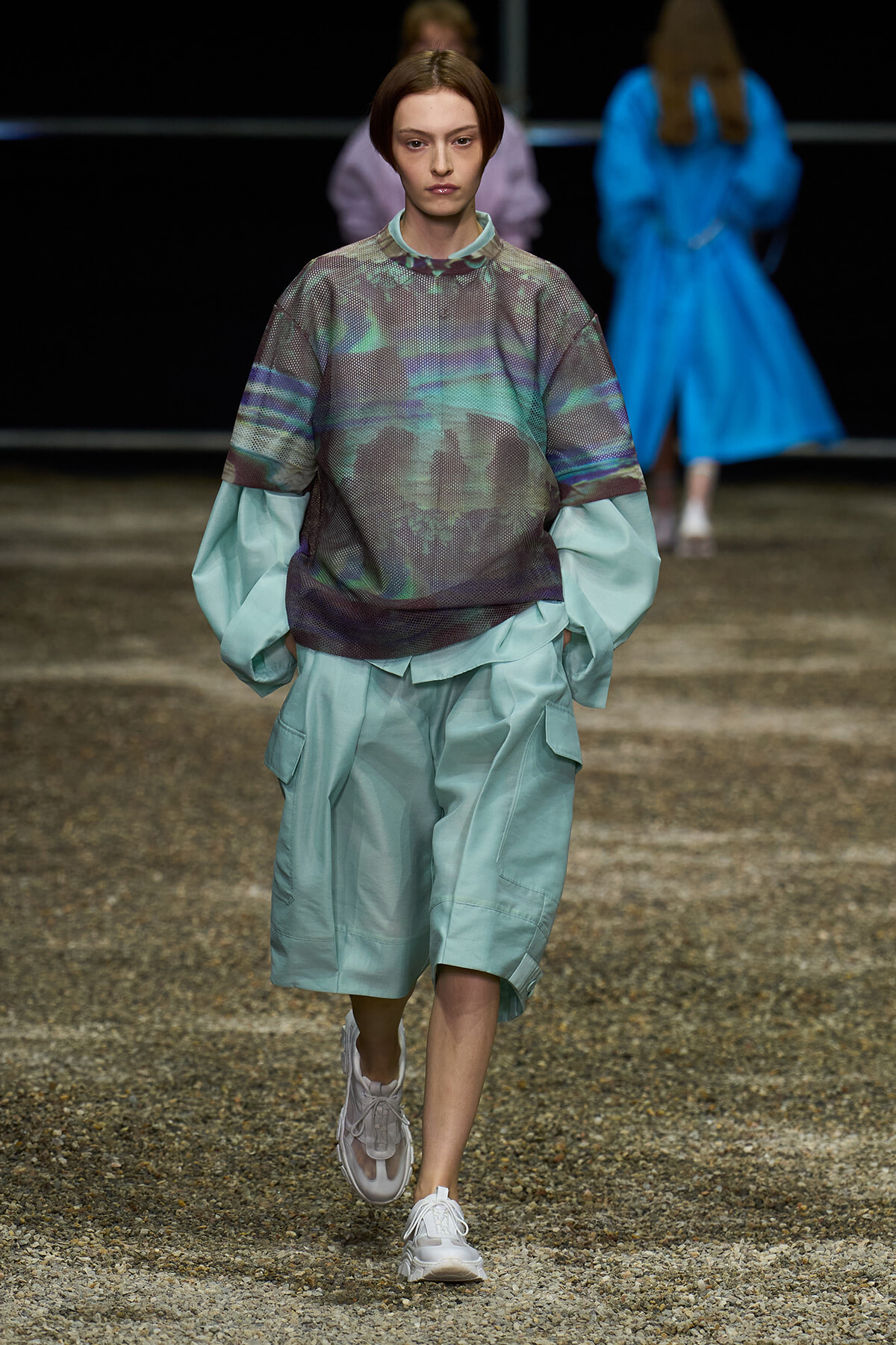 Model walks the runway in oversized mint cargo shorts with a layered mint top featuring a translucent, abstract print; white sneakers complete the look (fashion show).