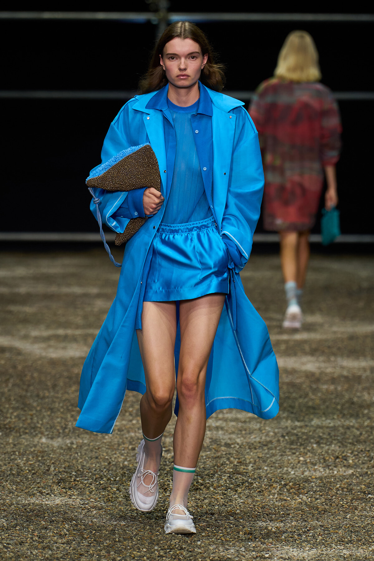 Model walks a blue monochrome outfit down the runway, clutching a brown textured tote.