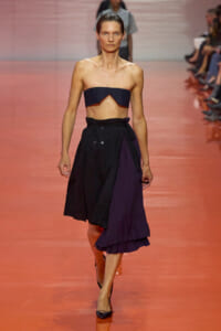 Model walking a runway in a navy strapless crop top and a high-waisted black-and-purple midi skirt.