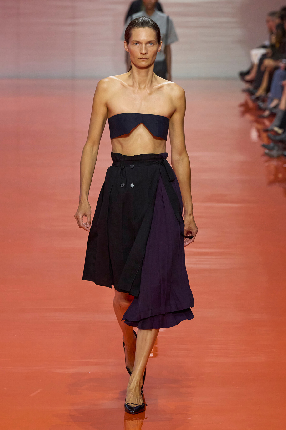 Model walking a runway in a navy strapless crop top and a high-waisted black-and-purple midi skirt.