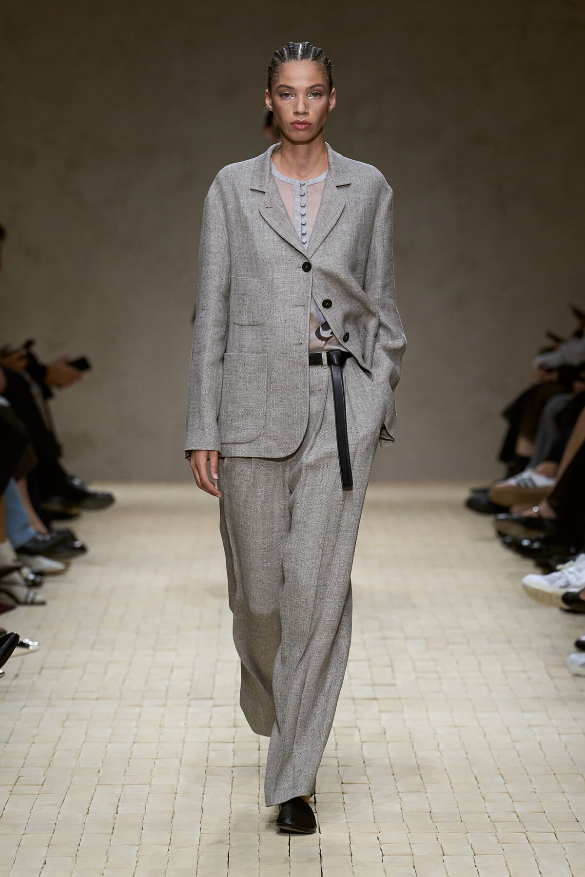 Model walks the runway in a light gray oversized suit: single-breasted blazer with large pockets and a thin belt over matching wide-leg pants.