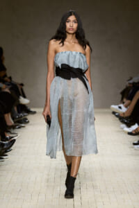 Model walking the runway in a light-blue strapless sheer midi dress with a thick black belt and lace-up black boots.