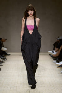 Model walks the runway in black, oversized, halter-style jumpsuit over a pink sequined bandeau top.