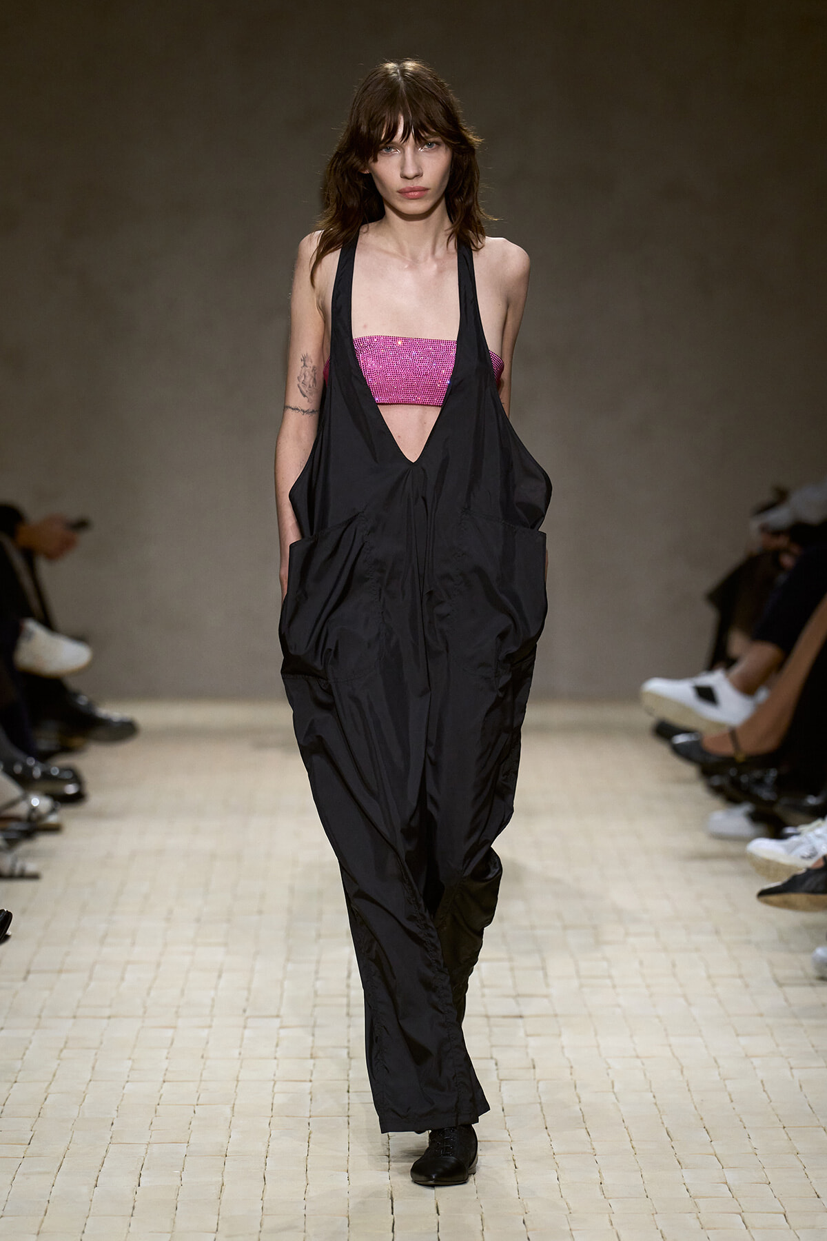 Model walks the runway in black, oversized, halter-style jumpsuit over a pink sequined bandeau top.
