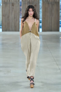 Female model walks a fashion runway wearing a two-tone beige/brown jumpsuit with rope ties and platform sandals.