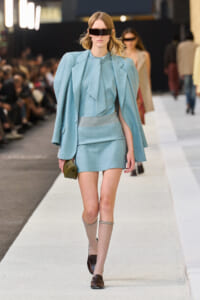 Runway model in a pastel blue tailored suit with an oversized blazer and matching miniskirt, wearing large rectangular sunglasses.