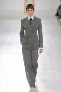 Model walks the runway in an oversized gray double-breasted suit with a white shirt and dark tie.