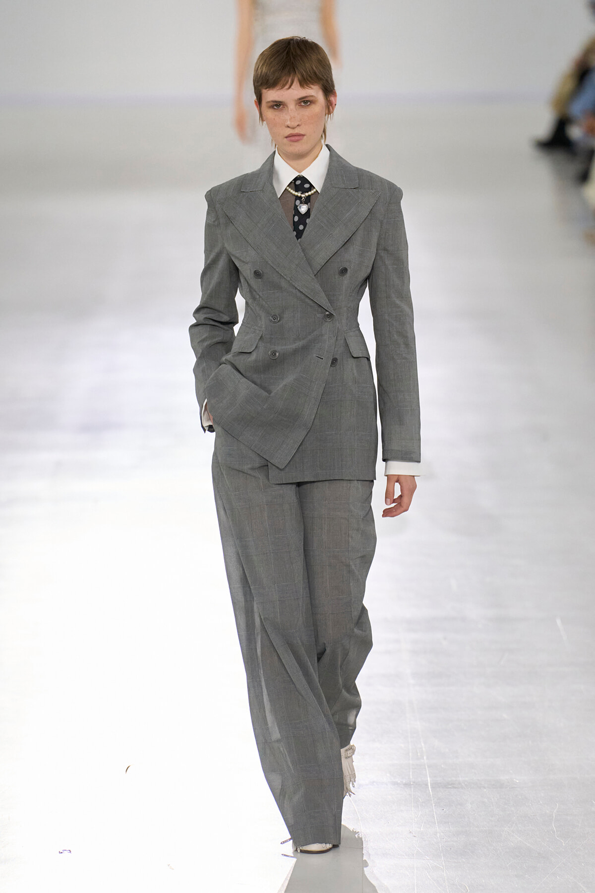 Model walks the runway in an oversized gray double-breasted suit with a white shirt and dark tie.