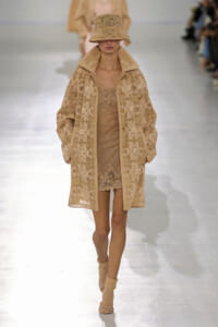 Model walks a beige lace coat over a sparkling beige dress, matching wide-collar coat, bucket lace hat, on a runway.