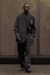 Man wearing a dark pinstripe suit with a blue pocket square, walking toward the camera.