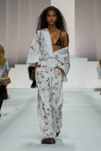 Model walks the runway in a light-blue striped floral loungewear set, unbuttoned at the top to reveal a black lace bralette.