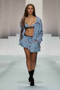 Model walks the runway in a blue striped floral pajama set with a lace-trimmed bralette and a burgundy handbag.