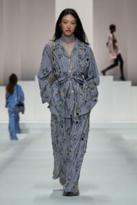 Model walking runway in striped floral-embellished suit with belt, lace turtleneck underneath.