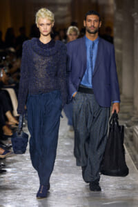 Two models walk a runway in coordinated blue outfits; textured knit top with wide pants and a blue blazer look.