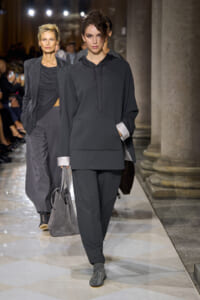 Model in oversized charcoal-gray hoodie and matching joggers walks the runway, carrying a gray suede tote.