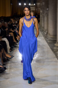 Model walks the runway in a royal blue draped slip dress with a chunky blue beaded necklace.
