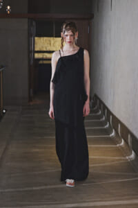 Woman in a black one-shoulder, floor-length gown walking down a dim hallway.