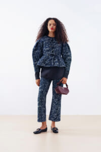 Woman with curly hair wearing a navy floral peplum top and matching wide-leg pants, black loafers, and a burgundy handbag.