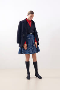 Model wearing a navy blazer over a red shirt with a blue floral A-line skirt, knee-high socks, and black flats against a light backdrop.