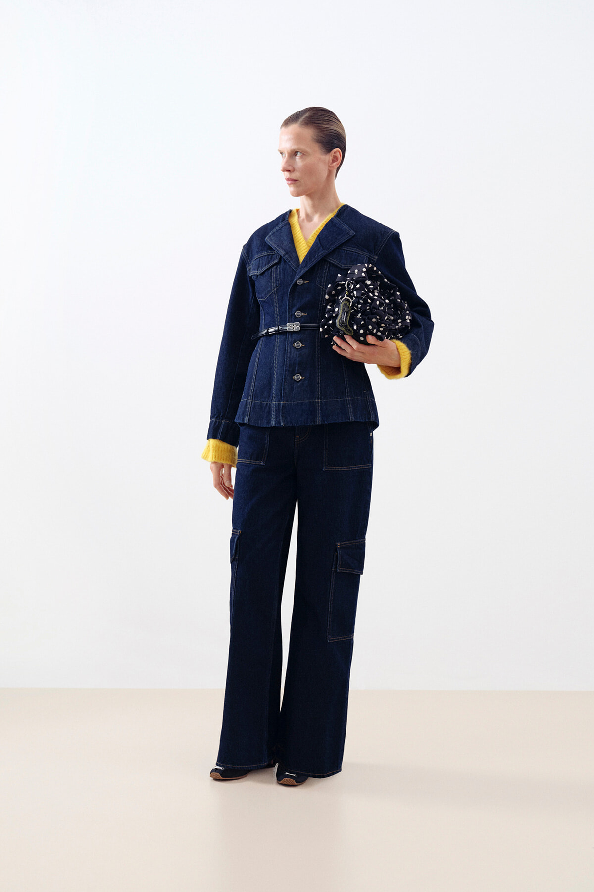 Full-body shot of a person in a dark denim suit with yellow cuffs, holding a black-and-white patterned bag.