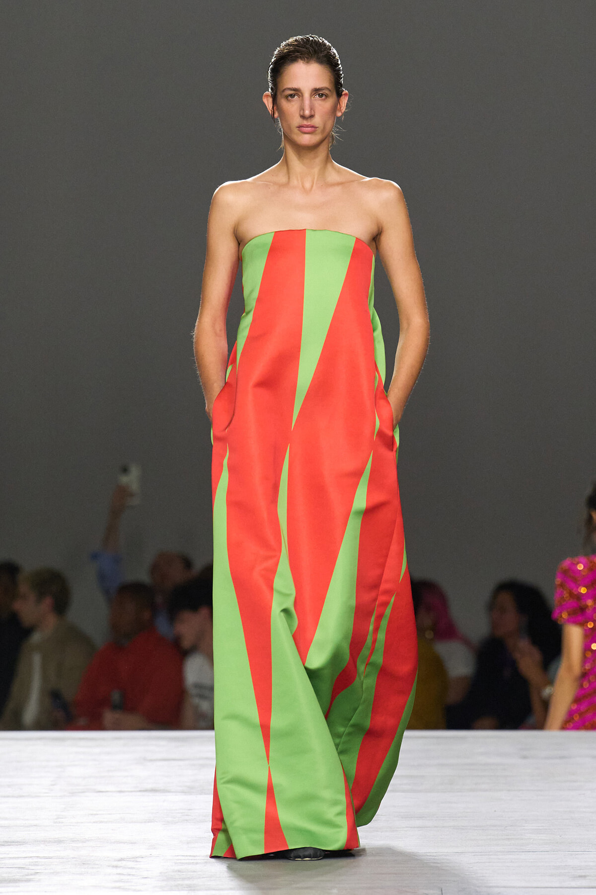 Strapless, floor-length dress with bold red and lime green geometric panels worn by a model on a runway.