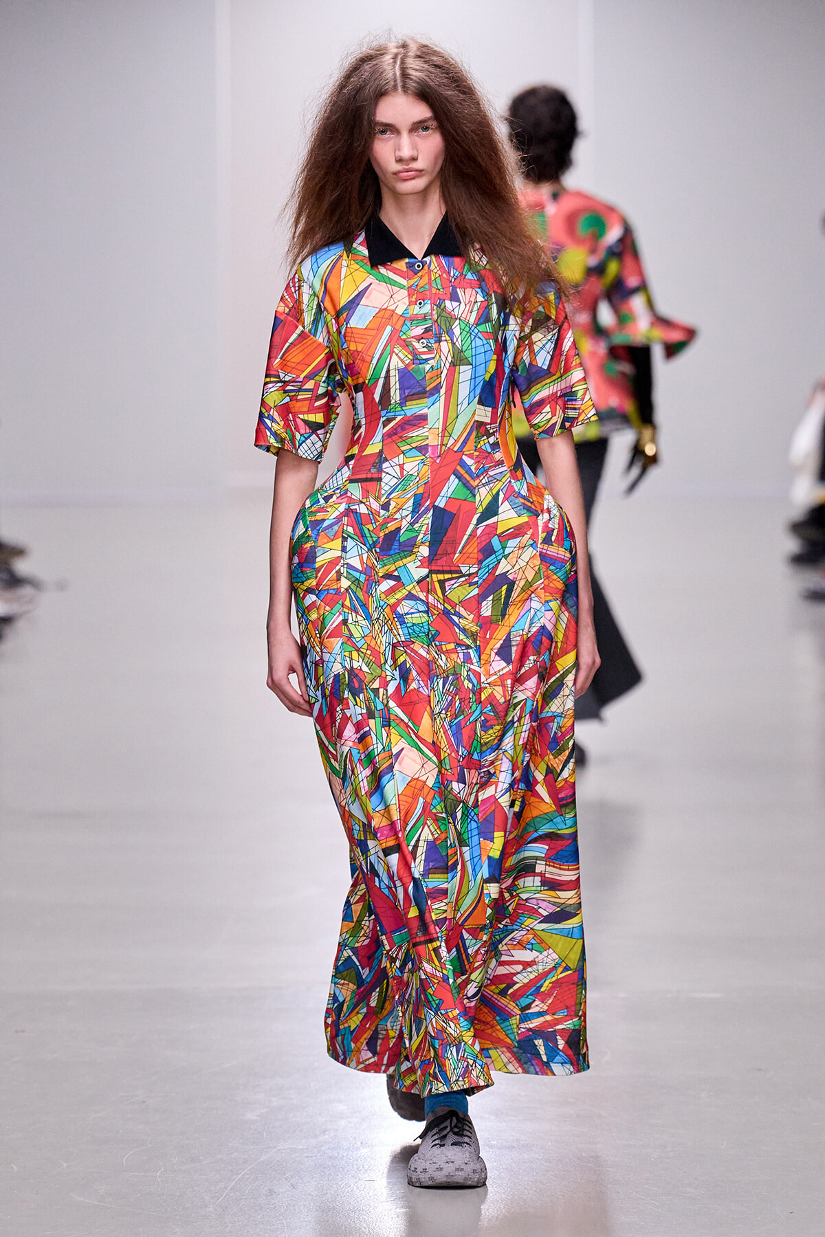 Runway model wearing a floor-length, multicolor geometric print dress with a black collar.