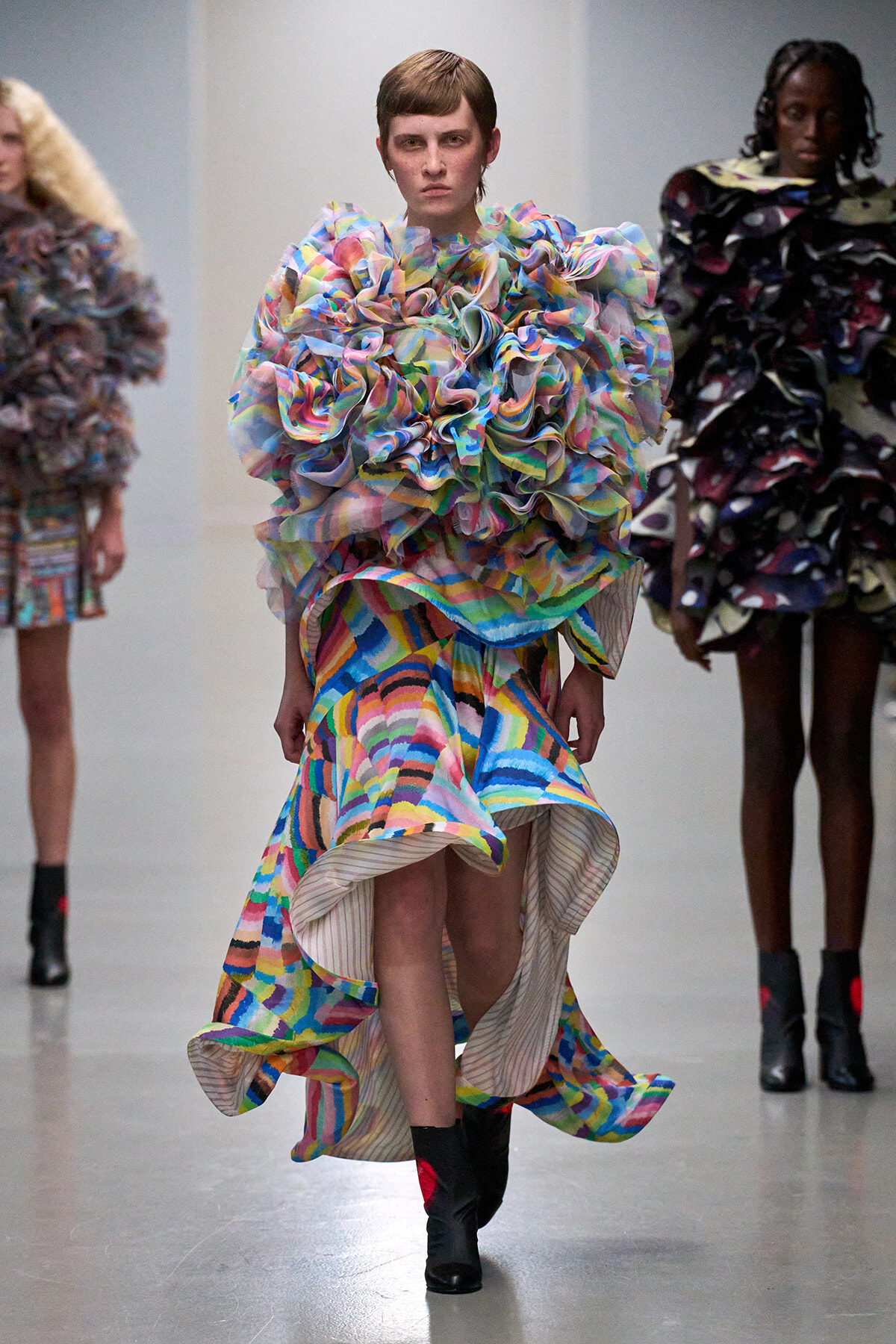 Model wearing a voluminous, multicolored ruffle gown on a runway.