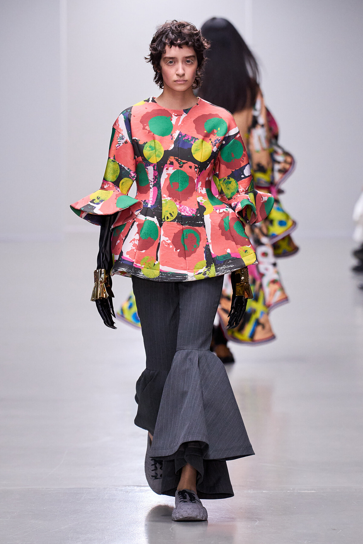 Model walks the runway in a bright abstract-print top with wide, flared sleeves and a dark gray layered skirt.