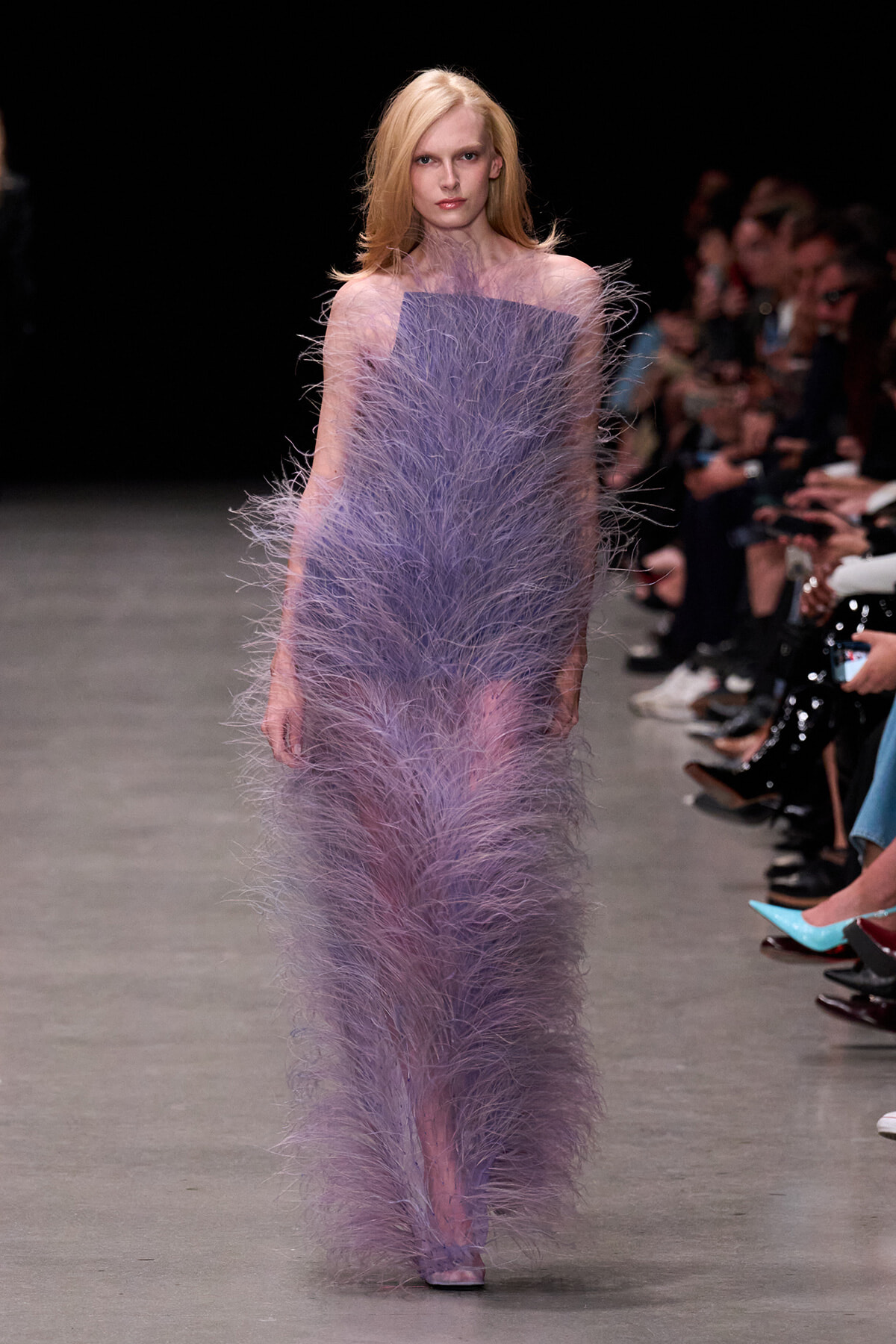 Model walks the runway in a lavender, feathered floor-length gown with bare shoulders.